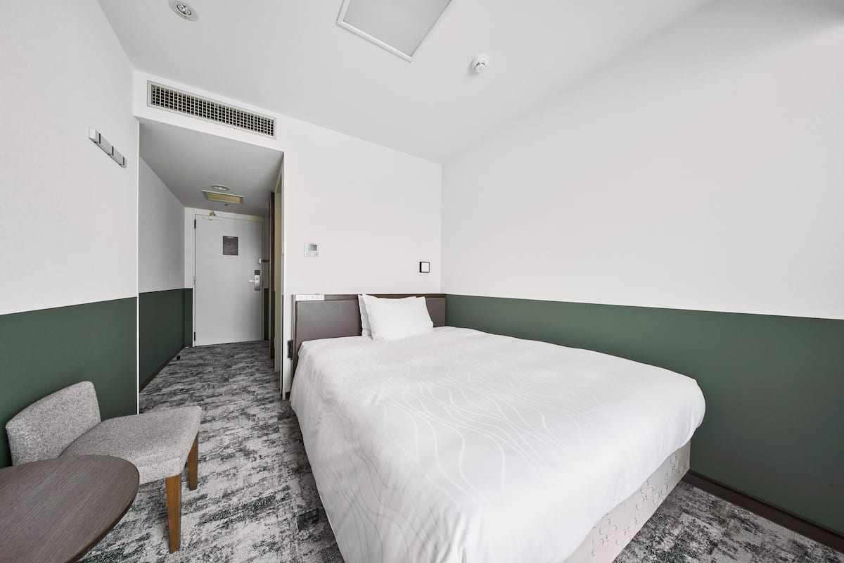 A hotel room with a large bed, a small desk, a chair, and a carpeted floor.