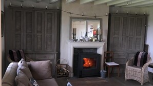 A cozy living room with a fireplace, a sofa, a wicker chair, and a dining table. - Charming 19th century country house   all comforts, great charm   true nature. (Ceaulmont)
