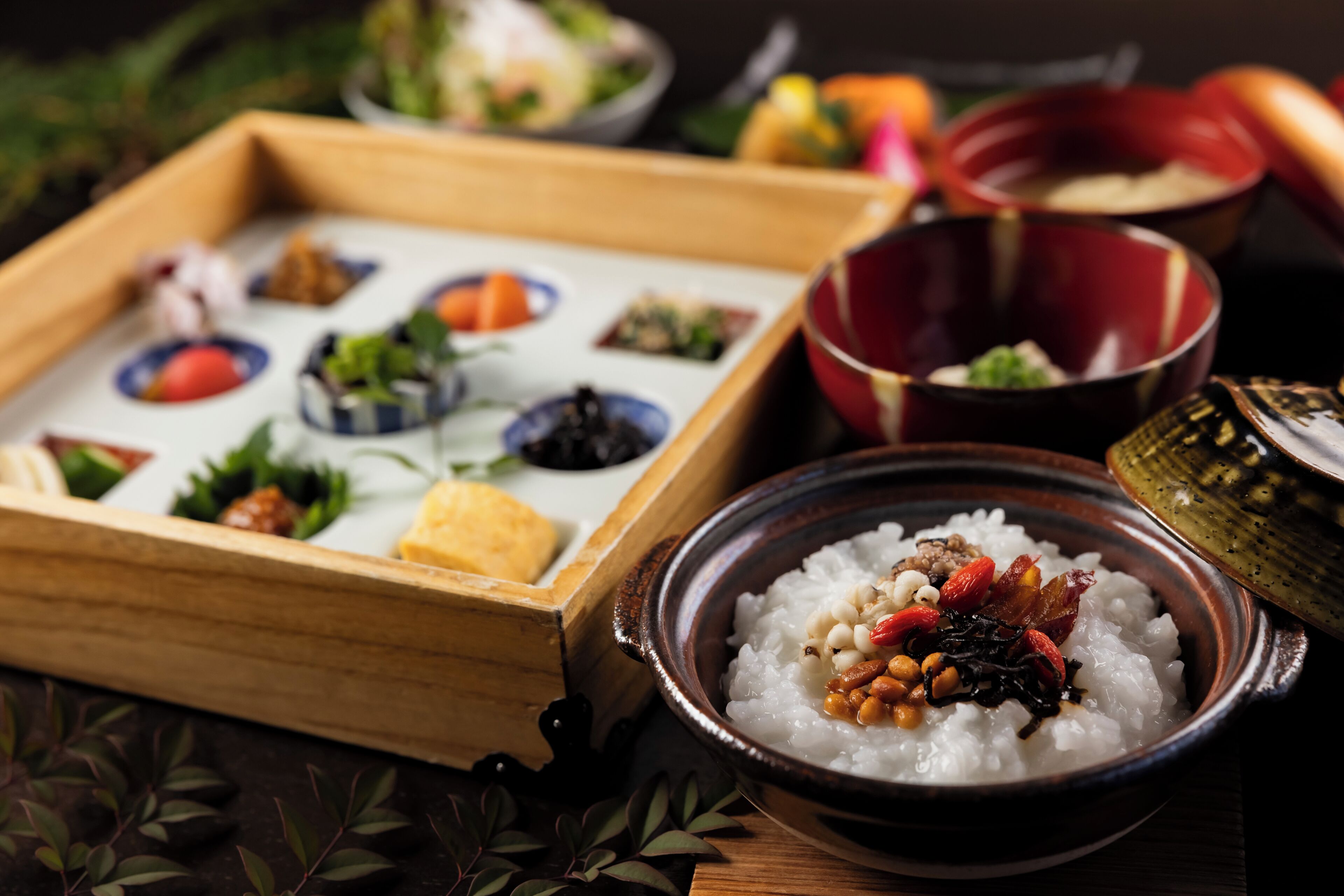 A wooden tray with various dishes, a bowl of rice with toppings, and a red bowl.