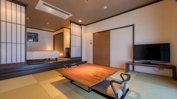 Una habitación de estilo japonés tradicional, con suelo de tatami, una cama baja de madera, un televisor sobre un mueble y puertas correderas.