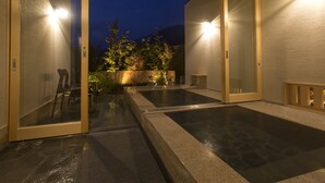 A modern building with a glass entrance, a patio area with a stone floor, and a view of a mountain at dusk. - Yufuin Onsen Toshoan (Yufu)