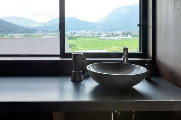 Un baño con un ventanal grande, un lavabo de piedra y una cafetera.