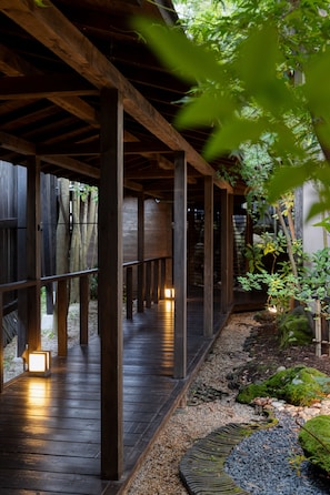 A wooden deck with a railing, surrounded by greenery and a stone pathway. - Yufuin Onsen Toshoan (Yufu)