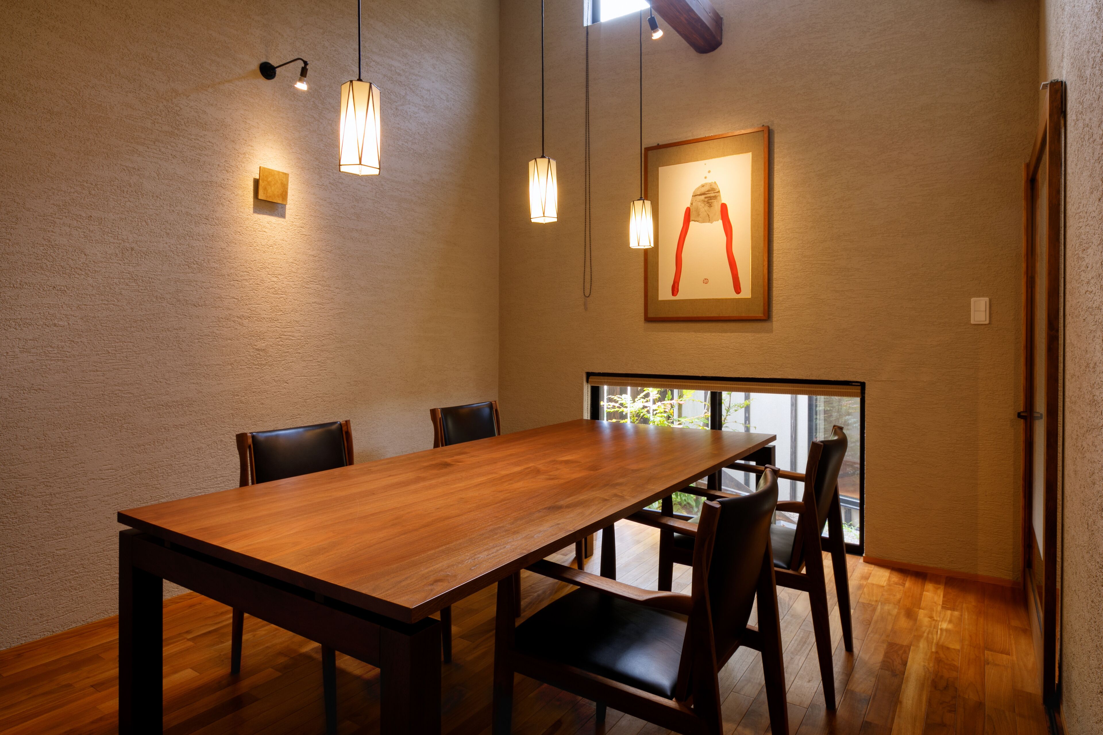 A dining area with a wooden table and chairs, pendant lights, and a framed artwork on the wall.