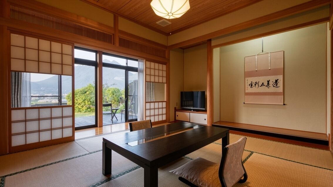 A traditional Japanese room with tatami flooring, a low table, sliding doors, a television, and a framed calligraphy piece.