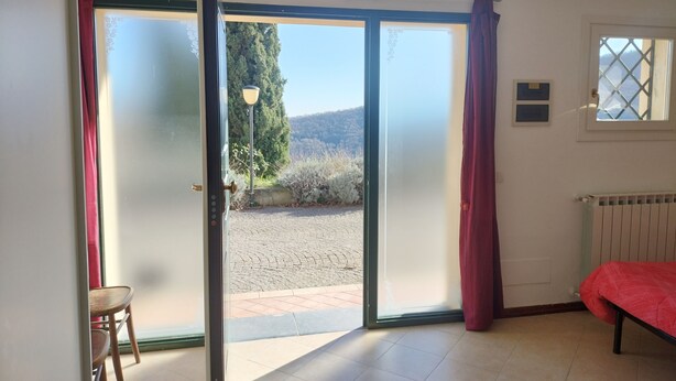 A room with a bed, a chair, and a sliding glass door leading to an outdoor area with a view of trees and a mountain.