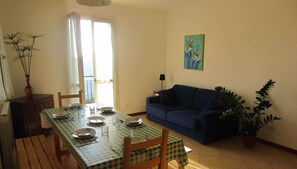 A dining area with a table set for four, a sofa, a potted plant, and a painting on the wall.