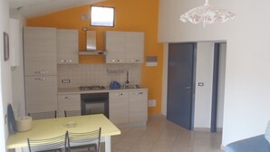 Cocina compacta con armarios blancos, una mesa de comedor amarilla y una puerta azul.