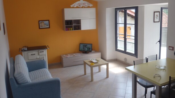 Sala de estar con un sofá azul, una mesita de madera, un armario blanco y un ventanal con vista a un edificio.