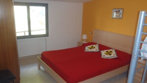 Un dormitorio con cama, ventana, mesita de noche, lámpara y un cuadro en la pared.
