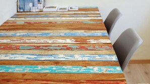 Una larga mesa de madera con pintura descascarada, rodeada de sillas.