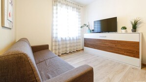 Una sala de estar moderna con un sofá, un televisor sobre un mueble de madera y una ventana con cortinas.