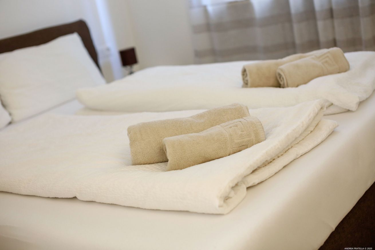 A neatly made bed with white linens and beige towels.