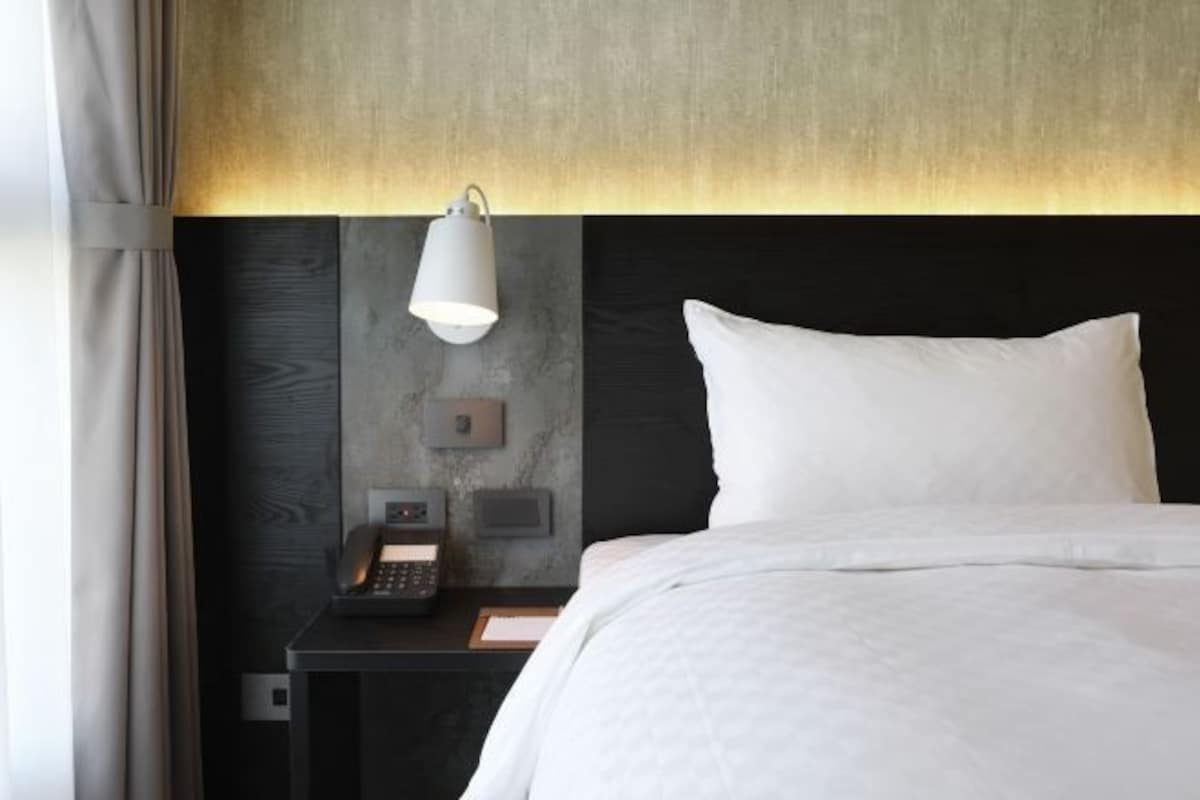 Une chambre d’hôtel comprenant un lit, une table de chevet avec une lampe, un téléphone et un panneau de commande fixé au mur.