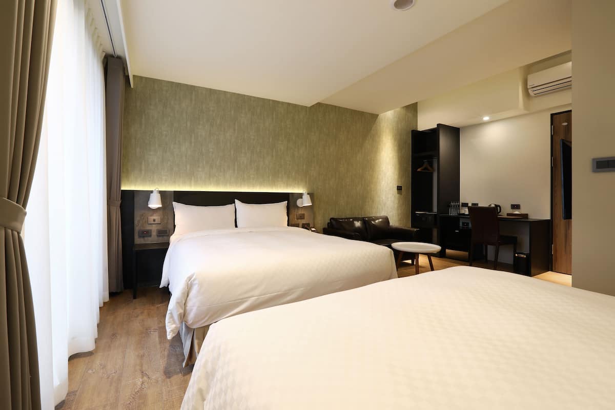 Hotellihuone, jossa on kaksi sänkyä, työpöytä, tuoli, pieni pöytä ja peili.