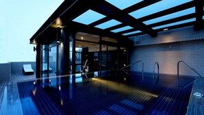 Une piscine intérieure moderne avec des murs en verre, une terrasse en bois et un espace couvert avec des sièges.