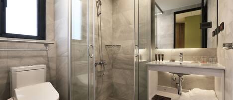 Un baño moderno con ducha envuelta en vidrio, inodoro y tocador con lavamanos y espejo.