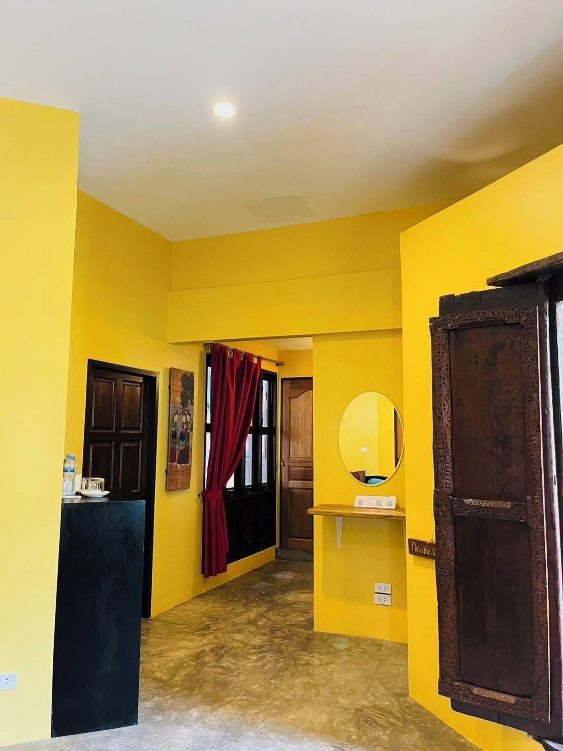 A hallway with yellow walls, a wooden door, a mirror, and a red curtain.