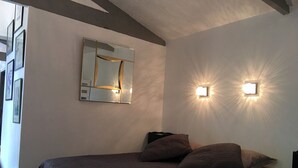 A bedroom with a bed, a wall-mounted mirror, and two wall sconces. - Charming mazet for 4 pers. 33m2 swimming pool (Saint-Paul-De-Vence)