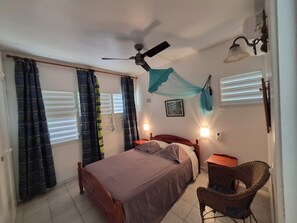 A bedroom with a bed, a ceiling fan, a chair, and a window with curtains.