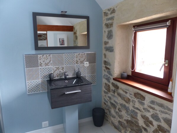 A bathroom with a black sink, a mirror above it, patterned tiles, a stone wall, and a window with a towel rack. - Family room, 2 mins from the beach (Plouër-Sur-Rance)