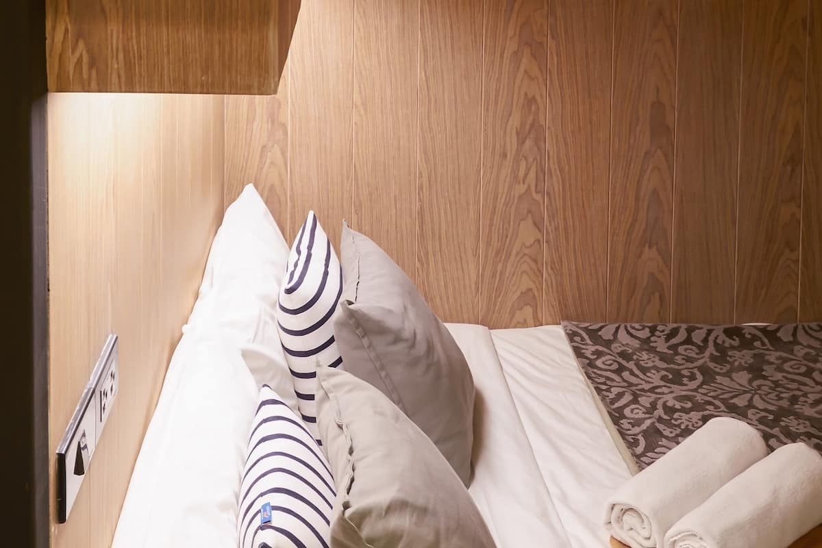 A bunk bed with a wooden headboard, white bedding, and striped pillows.