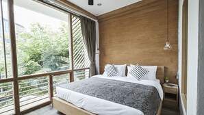 A modern bedroom with a large window, a wooden headboard, and a bedside table with a plant. - Vann Bangkok Boutique House (Bangkok)
