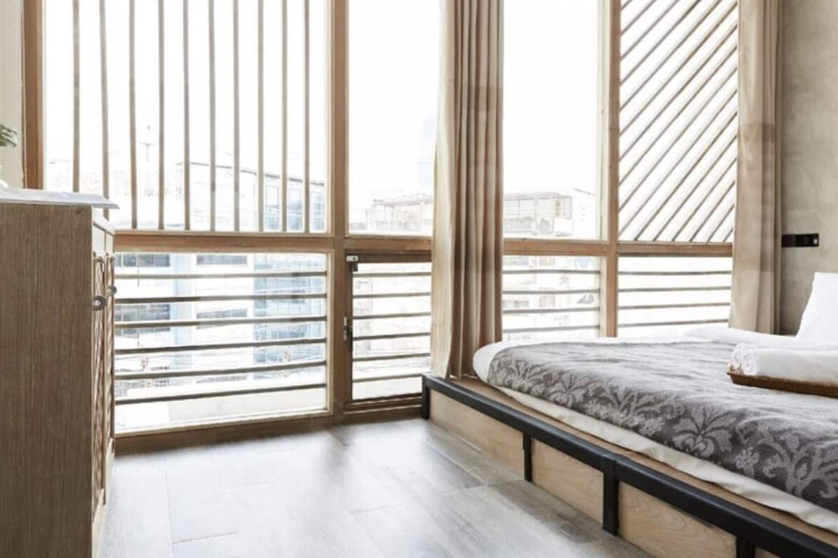 A modern bedroom with a large window, a bed with a patterned bedspread, and a wooden bench.