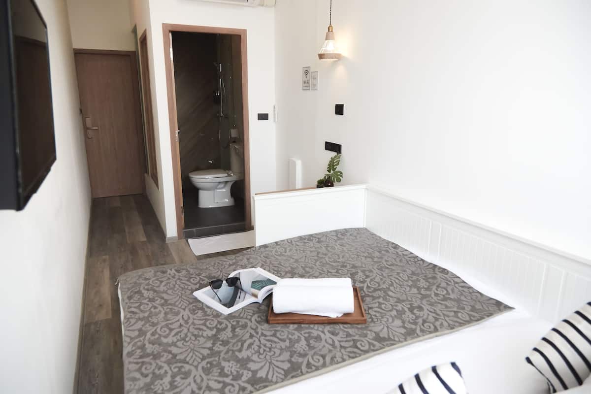 A compact hotel room with a bed, a small bathroom, and a visible shower area.