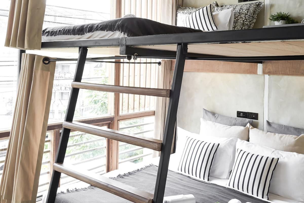 A bunk bed with a ladder, a bedside table with a plant, and a window with curtains.