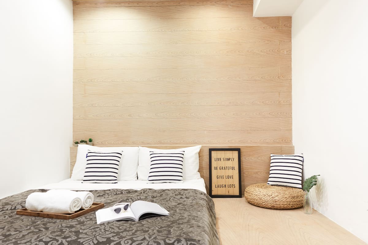 A neatly made bed with a patterned bedspread, a tray with rolled towels, and a framed inspirational quote on the wall.