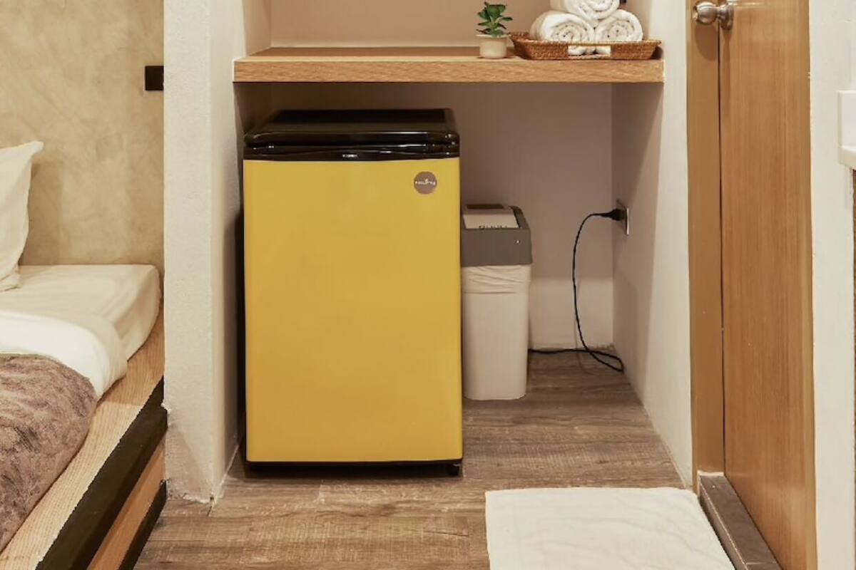 A compact room with a bed, a small yellow refrigerator, and a wooden door.