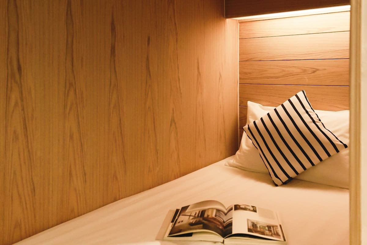 A small, cozy room with wooden walls and a single bed with a striped pillow and a book on it.