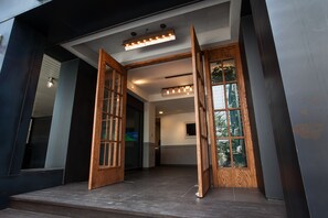 Une entrée moderne avec des portes en bois, un luminaire et une vue sur l’intérieur.