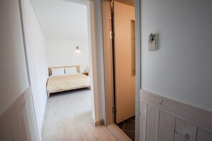 A narrow hallway with a bed at the end, a door with a handle, and a light switch on the wall.