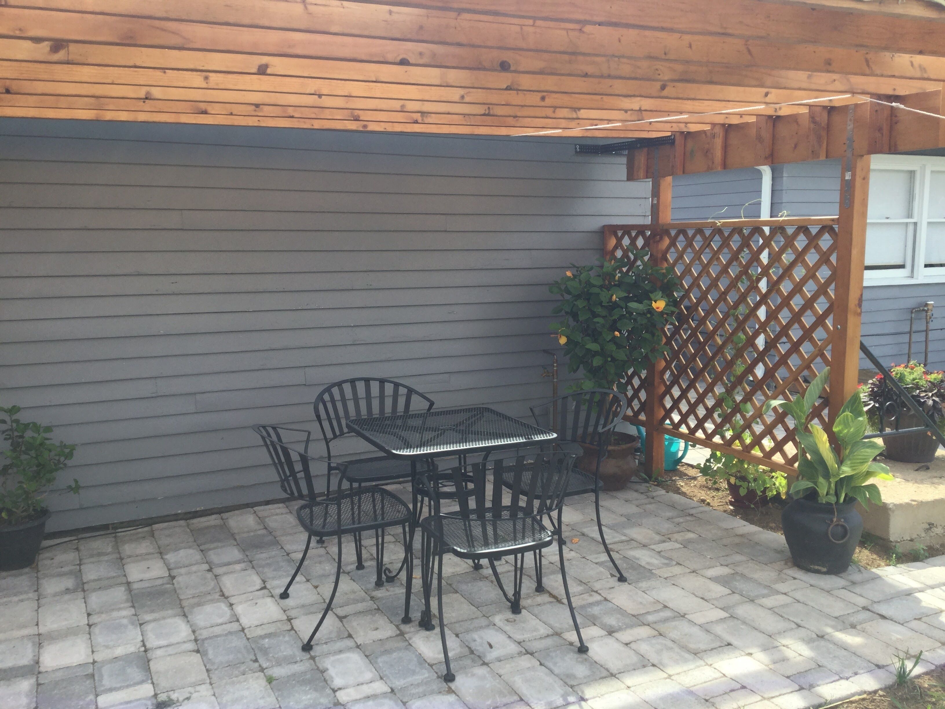 A patio with a metal table and chairs, a wooden pergola, and potted plants.