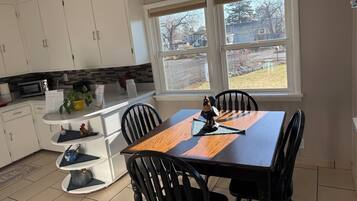 A modern kitchen with white cabinets, a dining table with chairs, and a view of the outdoors through a window.