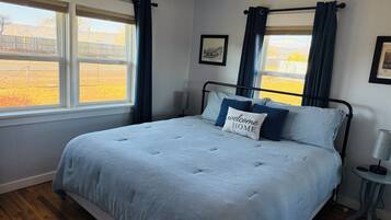 A bedroom with a bed, a bedside table, a lamp, and a window with curtains.