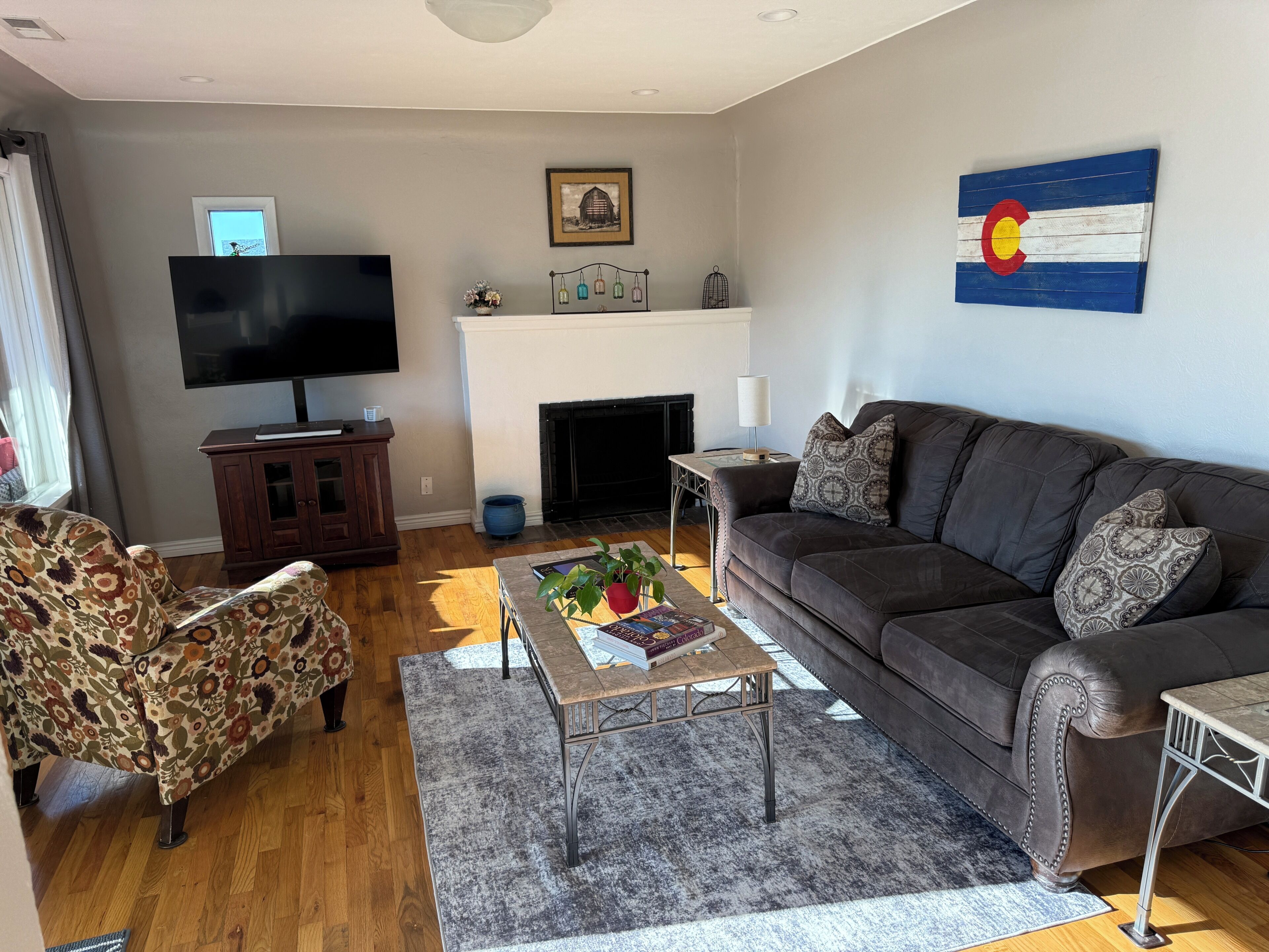 Een woonkamer met een bank, fauteuil, salontafel, flatscreen televisie, open haard en decoratieve wanddecoratie.