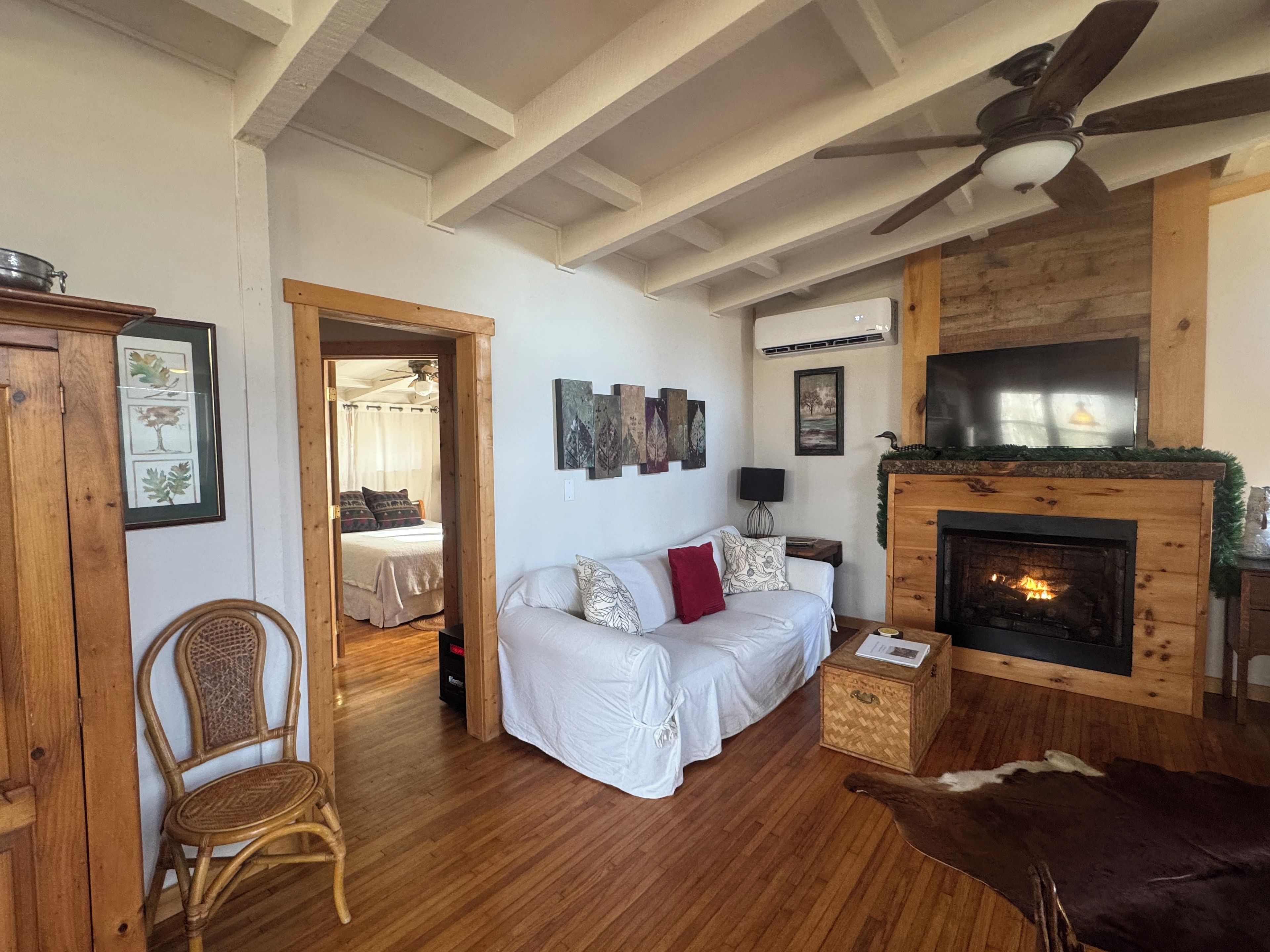 Un salon chaleureux avec une cheminée, un canapé, un plancher en bois et un ventilateur de plafond.