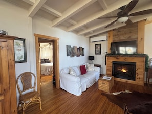 A cozy living room with a fireplace, a sofa, a wooden floor, and a ceiling fan.