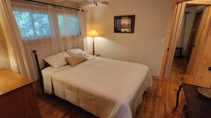 A bedroom with a bed, a bedside lamp, a framed picture on the wall, and a wooden door.