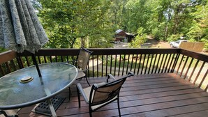 A wooden deck with a glass table and two chairs, surrounded by trees and a small cabin in the background. - Elk Ridge - cherokee casino GSMNP (Whittier)