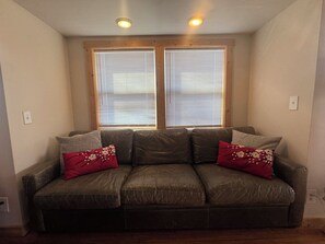 A room with a brown leather sofa, two windows with blinds, and a ceiling light fixture. - Elk Ridge - cherokee casino GSMNP (Whittier)