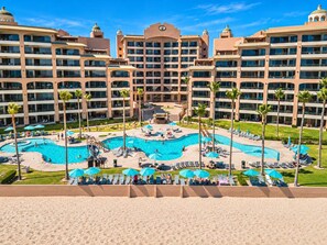 Un hôtel doté de plusieurs piscines, de palmiers et de chaises longues.