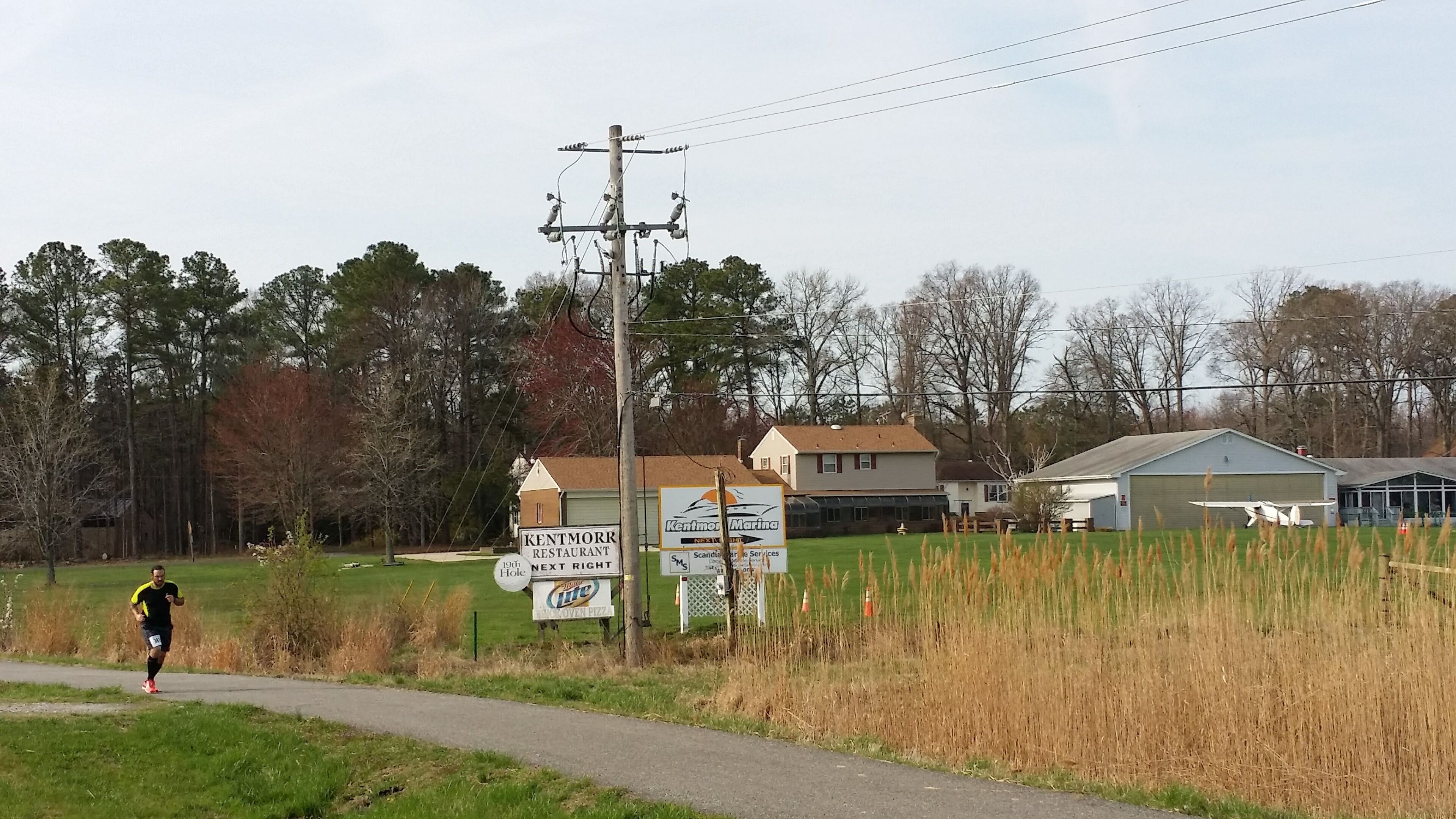 A rural road with a sign for Kentmor Restaurant and a small airplane on display.