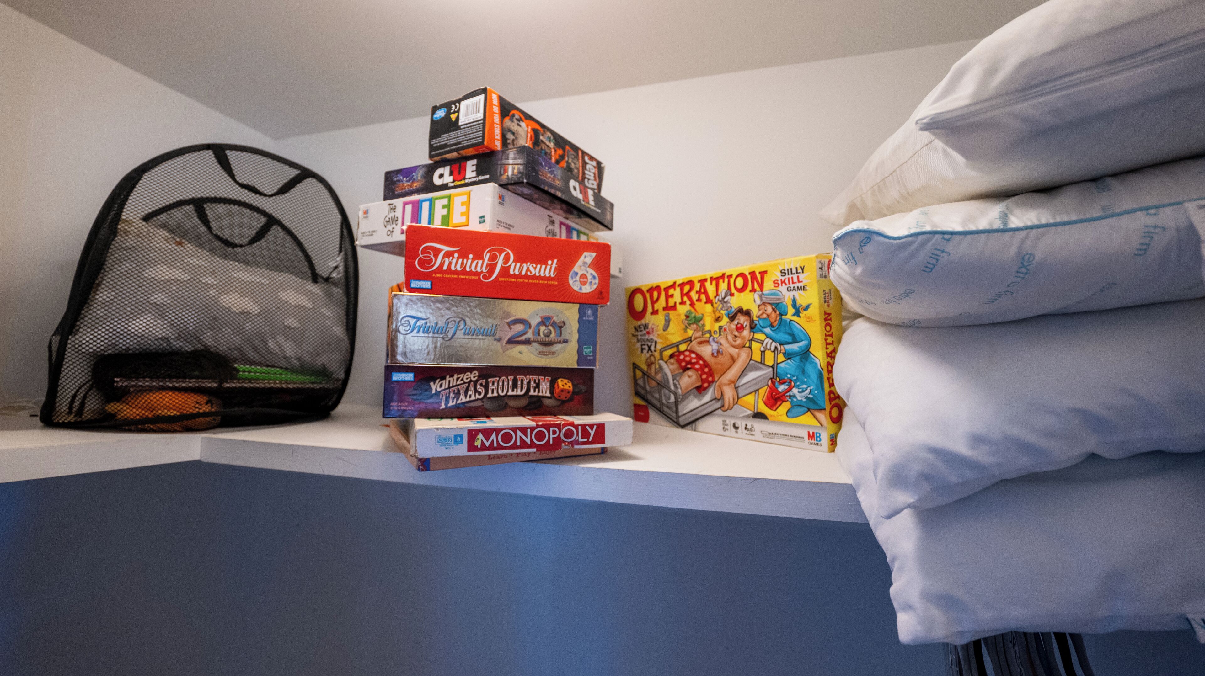 A stack of board games on a shelf, a mesh bag, and a pillow.