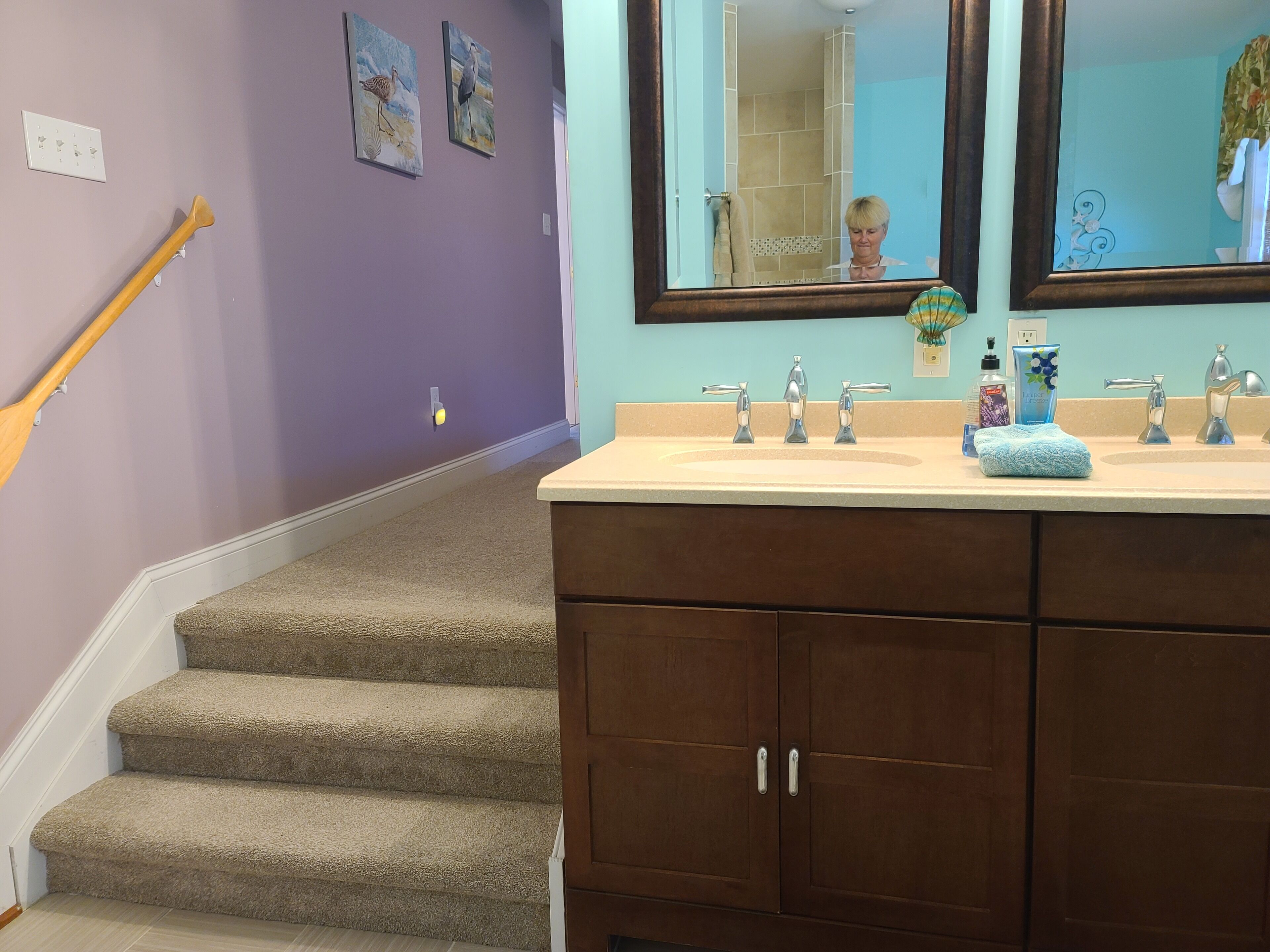 Un baño con lavamanos doble, un espejo y una escalera que lleva a otra habitación.