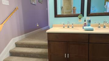Un baño con lavamanos doble, un espejo y una escalera que lleva a otra habitación.
