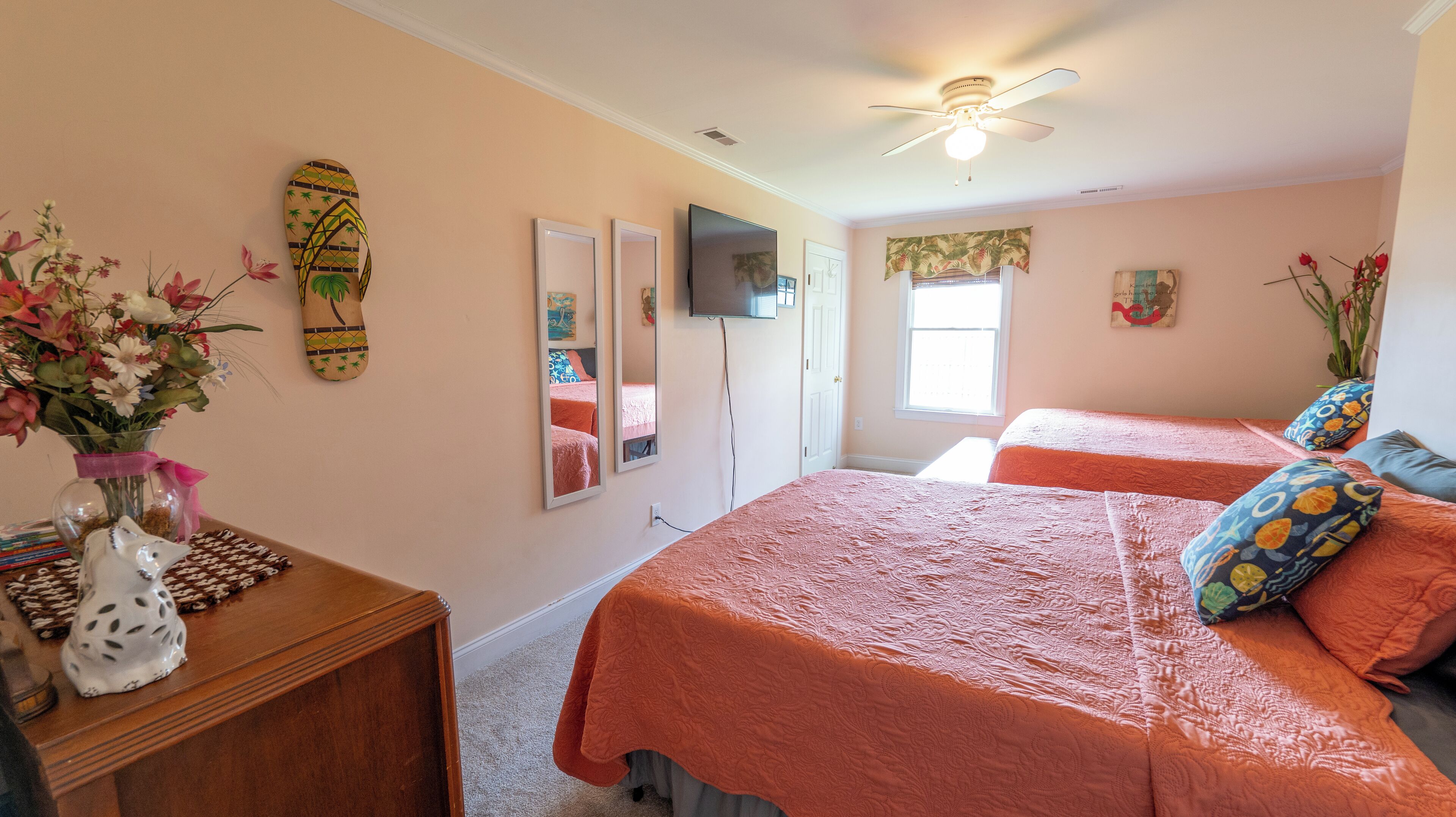 A bedroom with two beds, a ceiling fan, a TV, and a window.